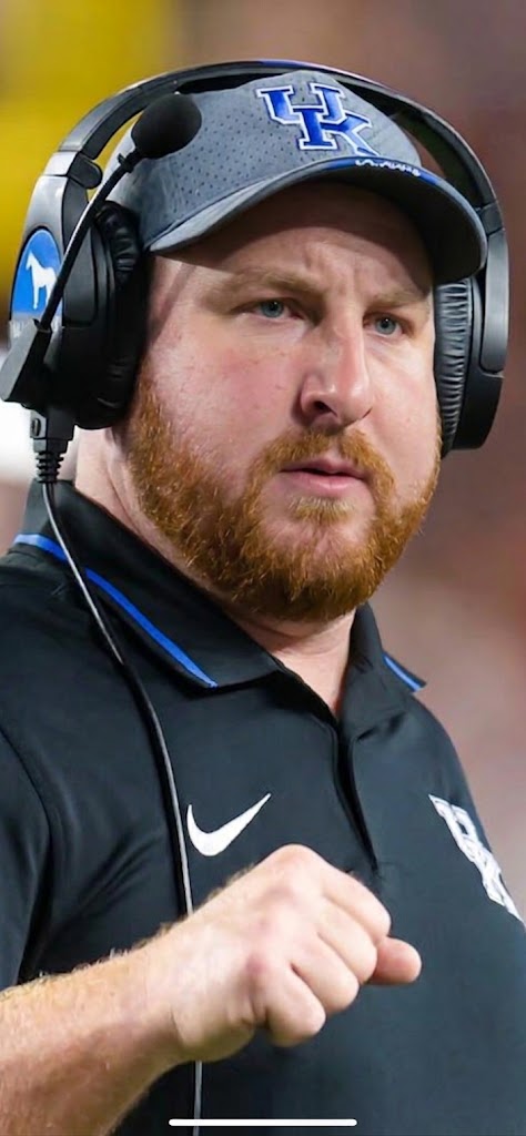 Coach in a Kentucky cap and headset pumping his fist on the sideline