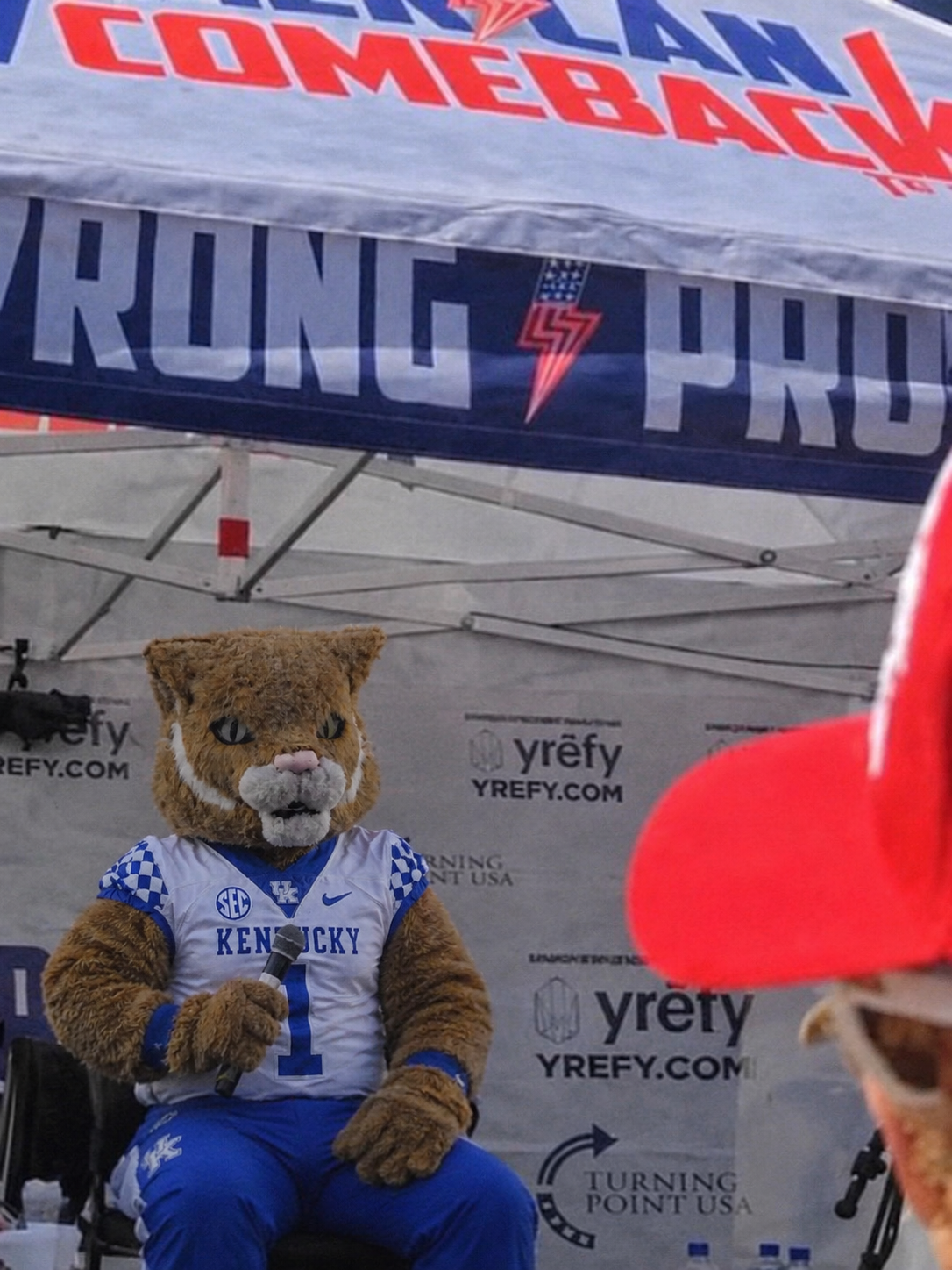 Kentucky Wildcat mascot on a mic at a campus tent